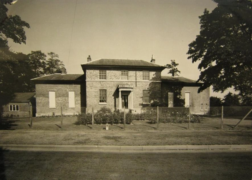 1964 photograph of the west-facing façade with rose beds and front borders
